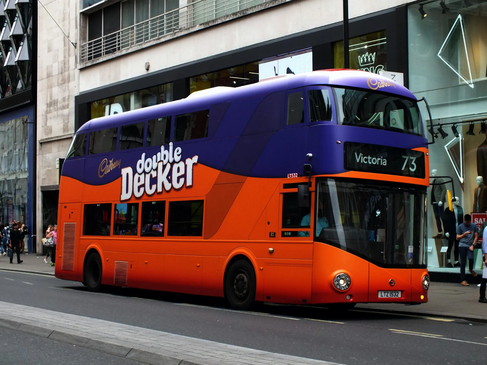 A London double decker bus showcasing a transit ad for the brand Cadbury UK, with the bus being wrapped as a double decker chocolate bar.